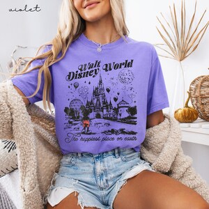 Puede incluir: Camiseta violeta con un gr&aacute;fico negro del castillo de Walt Disney World, Mickey Mouse y el texto "Walt Disney World" y "The happiest place on earth".