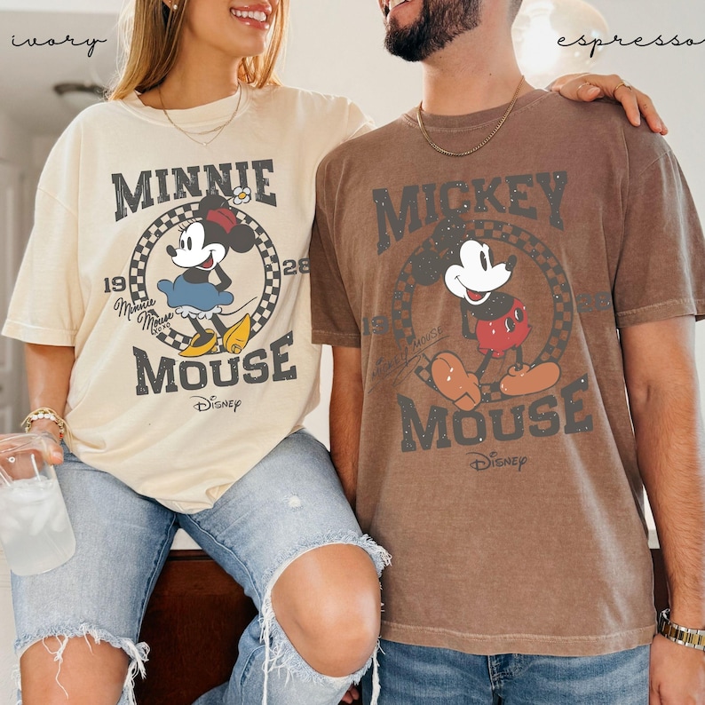 Puede incluir: Dos camisetas holgadas, una marfil y otra espresso, con Minnie y Mickey Mouse de Disney. La camiseta marfil muestra a Minnie Mouse con un vestido azul, mientras que la camiseta espresso muestra a Mickey Mouse con pantalones cortos rojos. Ambas camisetas tienen un dise&ntilde;o vintage.