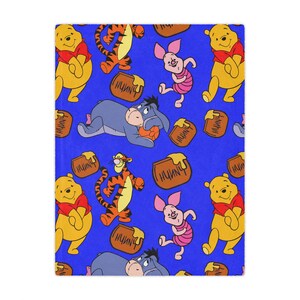May include: A blue blanket featuring a repeating pattern of Winnie the Pooh characters. The design includes Winnie the Pooh, Tigger, Piglet, and Eeyore, along with honey pots. The blanket is rectangular.