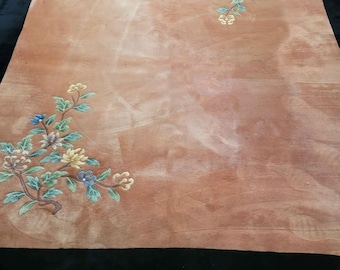Può includere: Un grande tappeto rettangolare con un centro color pesca e un bordo nero. Il tappeto presenta disegni floreali nei toni del blu, giallo e rosa. Il bordo è in materiale scuro e vellutato e il tappeto ha un bordo sfrangiato.