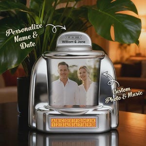 Op de afbeelding: Een zilverkleurige fotolijst in retrostijl met een foto van een stel. De lijst heeft de tekst "Personalize Name & Date" en "Custom Photo & Music". De bovenkant toont "William & Jane" en de datum "09-24-2025".