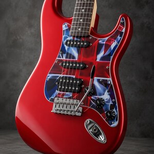 May include: A bright red electric guitar featuring a pickguard with a stylized Union Jack flag design. The instrument includes three pickups, a chrome tremolo bridge system, two black tone control knobs, and a maple neck with a dark fretboard.
