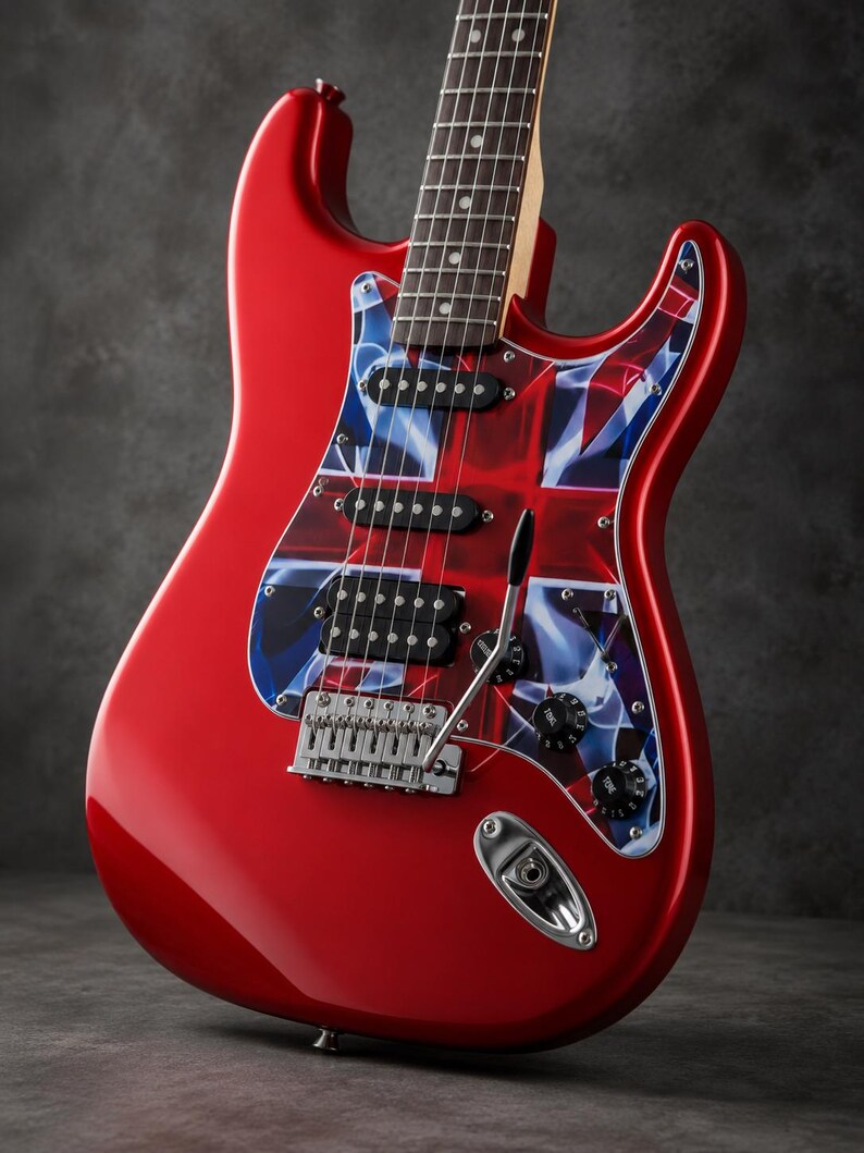 May include: A bright red electric guitar featuring a pickguard with a stylized Union Jack flag design. The instrument includes three pickups, a chrome tremolo bridge system, two black tone control knobs, and a maple neck with a dark fretboard.
