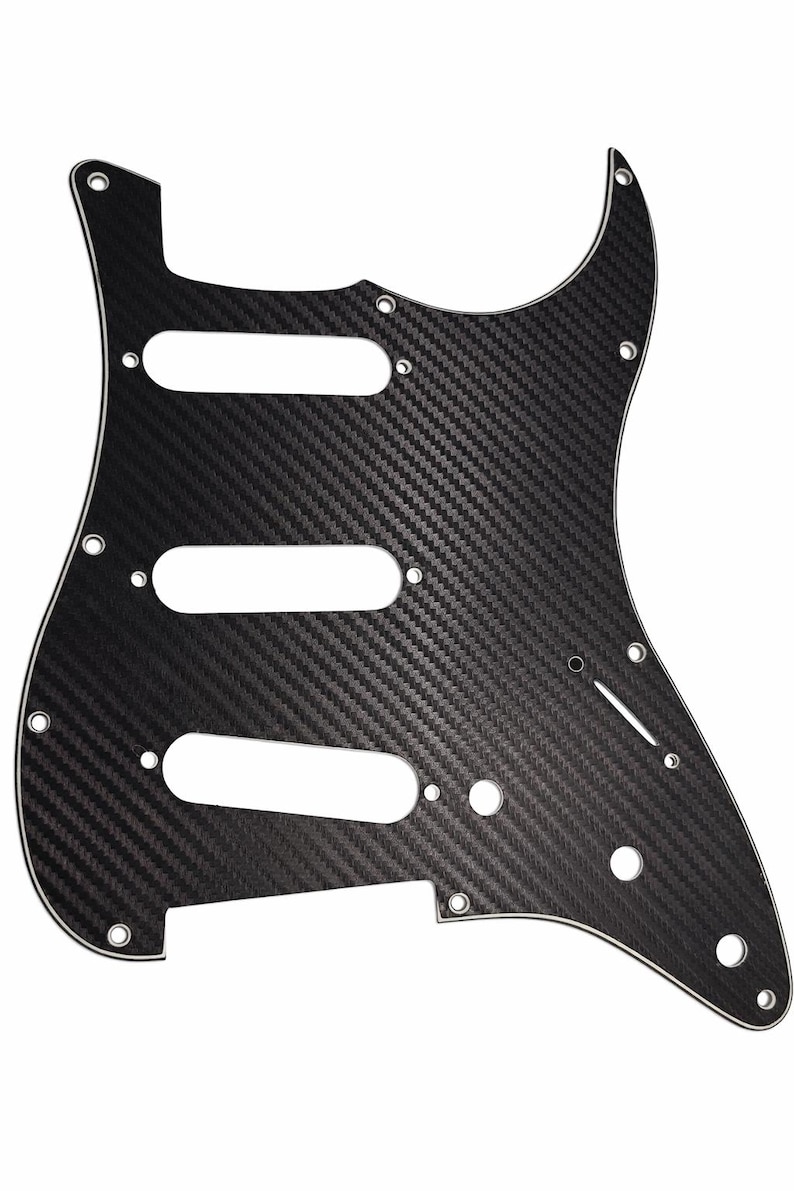 Puede incluir: Golpeador de guitarra de fibra de carbono negro con tres recortes para pastillas, una cavidad de control y orificios de montaje. El golpeador tiene una superficie texturizada y un borde blanco.