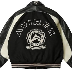 May include: Black and cream-colored varsity jacket with leather sleeves and a black body. The back features the word "AVIREX" in white lettering above a circular emblem that reads "PALACE LONDON SINCE 2009 ESTABLISHED 1975". The jacket has striped cuffs and a collar.