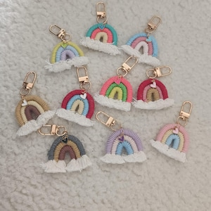 Puede incluir: Una colección de diez llaveros de arcoíris de macramé, cada uno con arcos de cordón de algodón multicolor, una base de flecos blancos y un mosquetón de metal dorado. Cada llavero está decorado con un pequeño dije en forma de corazón.