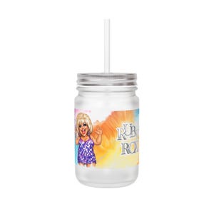 Könnte beinhalten: Ein klares Glas mit silbernem Deckel und weißem Strohhalm. Das Glas zeigt eine farbenfrohe Grafik einer Frau in einem lila Kleid mit dem Text "RUBY ROX". Der Hintergrund hat einen Batik-Effekt mit Orange-, Gelb- und Blautönen.