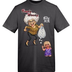 May include: Dark gray t-shirt featuring a cartoon illustration. The design includes a woman with white curly hair, glasses, and a leopard print top, holding a bag of white balls. The text "Bendy Wendy" and "RUBY ROX" are also visible.