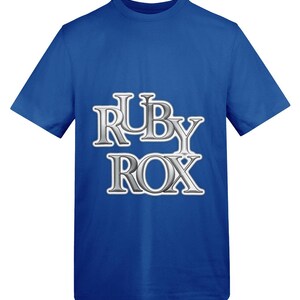 May include: Royal blue t-shirt with the text "RUBY ROX" in a silver, 3D-style font. The text is centered on the front of the shirt. The shirt has short sleeves and a crew neck.