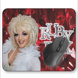May include: A mousepad featuring a woman with blonde hair, wearing a white feathered boa and a pearl necklace. The background is red with the text "RUBY BOX" and a black computer mouse.