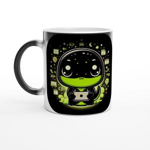 Può includere: Tazza in ceramica bianca con un disegno nero che cambia con il calore. Il disegno presenta un lucertola dei cartoni animati che tiene in mano un tablet, circondata da icone e una nuvola verde. Il manico è bianco.