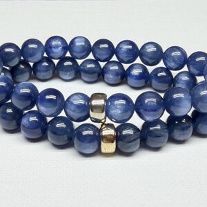 May include: Two beaded bracelets with dark blue, round beads. The bracelets are connected by two gold-colored spacers. The beads have a marbled appearance. The bracelets are displayed on a white surface.