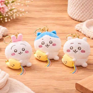 Peut inclure: Trois porte-clés en peluche avec des visages d'animaux de dessin animé. Chaque porte-clés a un corps blanc, des joues roses et une banane jaune. L'un a des oreilles bleues, l'autre des oreilles roses et l'autre des oreilles d'ours.