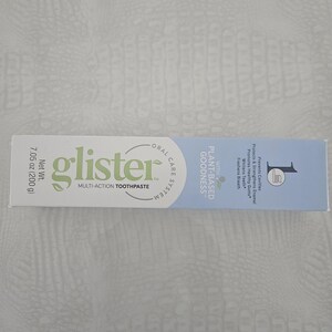 Op de afbeelding: Een tube "glister" multi-action tandpasta. De verpakking is wit met groene en blauwe accenten. De tekst op de tube bevat "Plant-Based Goodness" en "Netto gewicht 200 g". De tandpasta is ontworpen om gaatjes te voorkomen, glazuur te versterken en de adem te verfrissen.