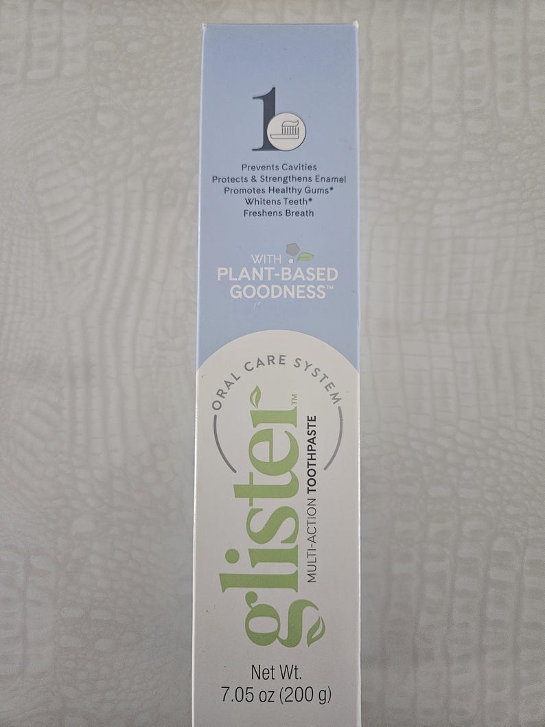 Op de afbeelding: Een lichtblauwe en witte doos met Glister multi-action tandpasta. De tekst luidt: "Voorkomt gaatjes, Beschermt & versterkt glazuur, Bevordert gezond tandvlees, Maakt tanden witter, Verfrist de adem." Netto gewicht: 200 g.