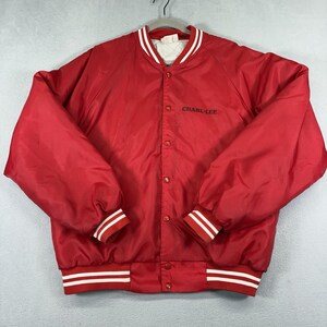 Puede incluir: Una chaqueta estilo varsity de color rojo brillante con cierre frontal de botones a presión, mangas largas y puños acanalados con rayas blancas. Incluye un cuello con rayas blancas y el texto CHARI-LEE bordado en negro en el pecho derecho.