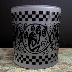 May include: A frosted glass tumbler with a black and white checkered pattern and a black silhouette design of stylized figures and vines.