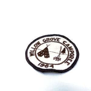 May include: A brown embroidered patch with white text that reads "Willow Grove Camporee 1964". The patch features a stylized image of a teepee and a campfire.