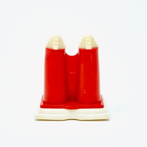 Puede incluir: Un molde de plástico rojo con una base blanca, diseñado para hacer dos formas idénticas. El molde tiene una parte superior texturizada y una parte inferior lisa.