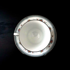 May include: A white teacup with a floral pattern on the rim. The cup is sitting on a saucer with a matching floral pattern.