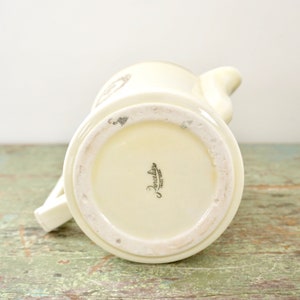 May include: White ceramic creamer with a gold trim and a floral design. The bottom of the creamer is marked "Porcelaine, Paris, France".