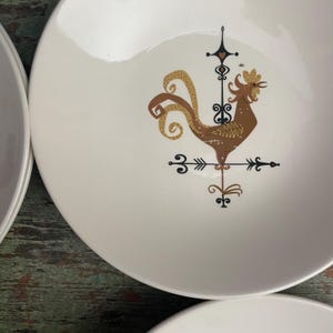 May include: White ceramic bowl with a brown rooster design. The rooster is on a weathervane with black and gold accents.