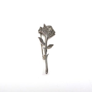 May include: A silver rose brooch with marcasite stones. The rose is detailed with a stem and leaves.