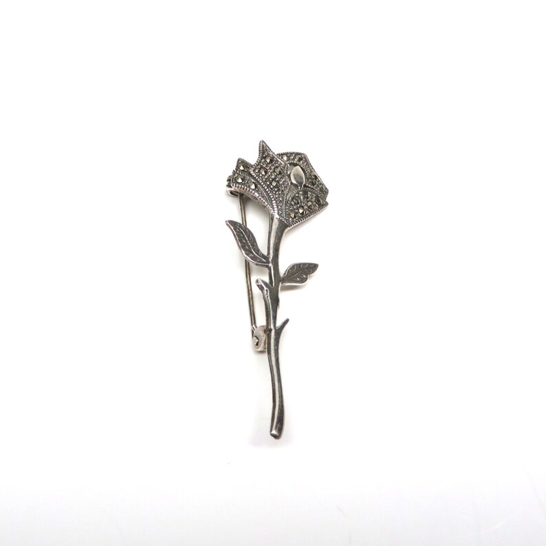 May include: A silver rose brooch with marcasite stones. The rose is detailed with a stem and leaves.