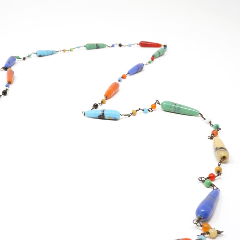 May include: A colorful necklace with long, teardrop-shaped beads in various shades of blue, green, orange, and yellow. The beads are strung on a thin wire with small, round beads in between.