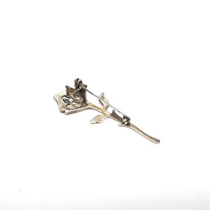 May include: A silver rose brooch with a detailed design. The rose is made of sterling silver and has a delicate stem and leaves.