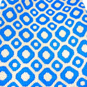 Puede incluir: Primer plano de una corbata con estampado azul y beige. La corbata presenta un dise&ntilde;o geom&eacute;trico repetitivo de formas de diamante azules con centros beige. La tela tiene una apariencia texturizada, lo que sugiere un material tejido. La est&eacute;tica general es moderna y elegante.