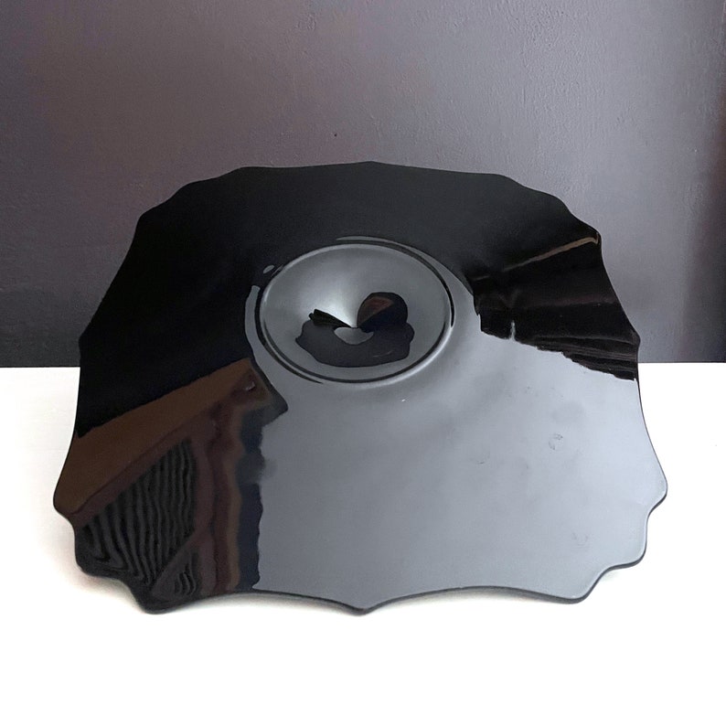 May include: A black, glossy, irregularly shaped serving dish with a central, circular depression.