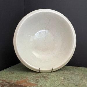May include: A white ceramic bowl with a crack running down the center. The bowl is sitting on a green wooden surface.