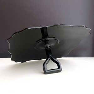 May include: A black glass cake stand with a scalloped edge and a handle. The stand is made of a glossy black glass and has a simple, elegant design.