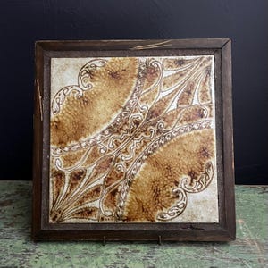 May include: A square ceramic tile with a brown and white geometric pattern, framed in a dark wood frame.