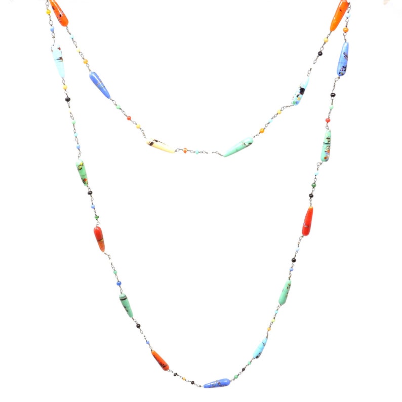 May include: A long silver chain necklace with colorful glass beads. The beads are shaped like teardrops and have a variety of patterns and colors, including red, orange, yellow, green, blue, and turquoise.