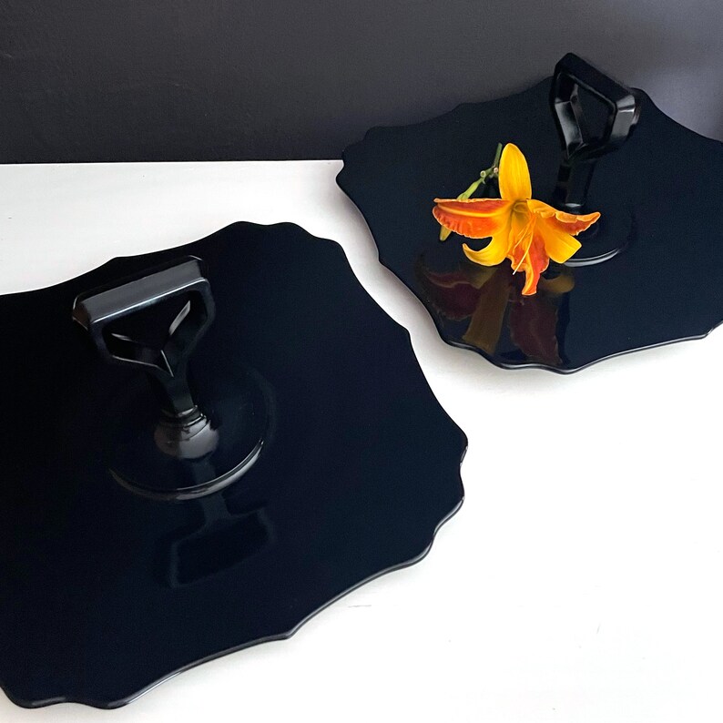 May include: Two black, scalloped serving trays with black handles. The trays are made of a glossy material and have a modern design.