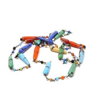 May include: A colorful glass bead necklace with a variety of colors, including blue, green, red, and orange. The beads are long and narrow, and they are strung on a silver chain.