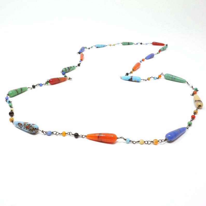 May include: A long necklace with a variety of colorful glass beads. The beads are teardrop shaped and have a variety of colors, including blue, green, orange, and yellow.