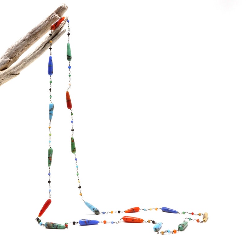 May include: A long necklace with a silver chain and colorful teardrop-shaped beads. The beads are in shades of red, orange, blue, green, and turquoise.