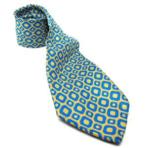 Puede incluir: Una corbata estampada en azul y dorado. La corbata presenta un dise&ntilde;o geom&eacute;trico repetitivo de formas azules sobre un fondo dorado. La corbata est&aacute; enrollada en la parte superior e inclinada hacia abajo, mostrando el patr&oacute;n y la textura.