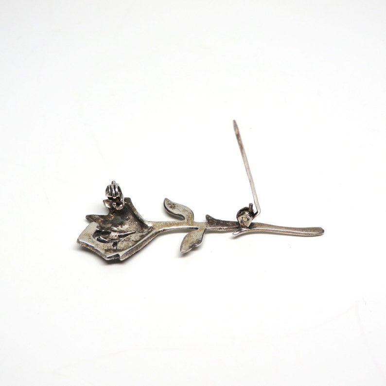 May include: A silver rose brooch with a black stone center and a pin on the back.