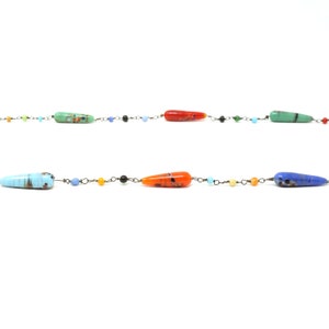 May include: A colorful glass bead necklace with a variety of colors, including blue, green, orange, and red. The beads are strung on a thin metal chain.