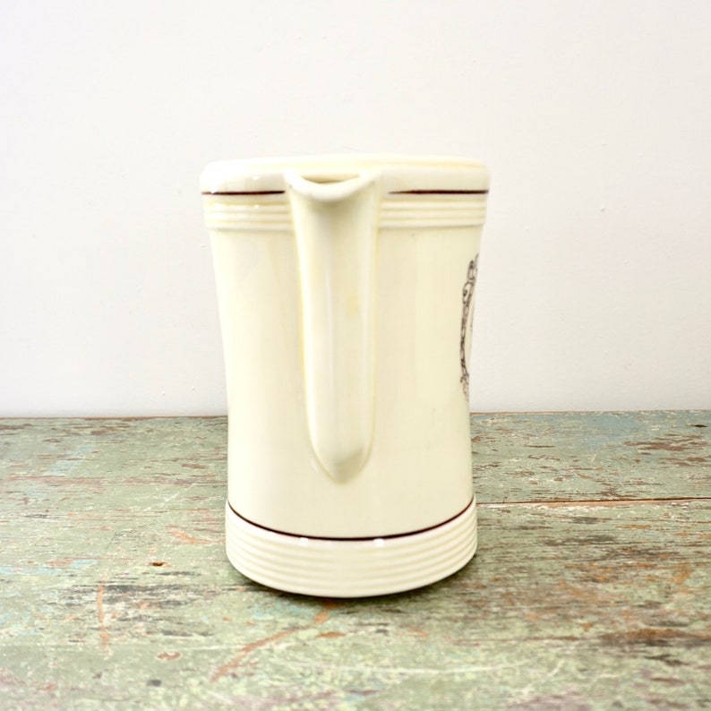 May include: A white ceramic pitcher with a brown rim and a decorative design. The pitcher has a handle and a spout.