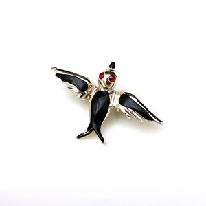 May include: A black and silver swallow brooch with red rhinestone eyes. The swallow is in flight with its wings spread.