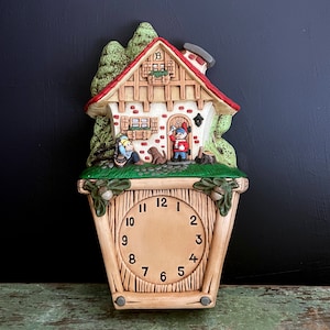 May include: A whimsical, vintage wall clock shaped like a cottage. The clock features a red roof, a brick facade, and miniature figures of gnomes. The clock face has black numbers and hands, and is surrounded by a wooden frame.