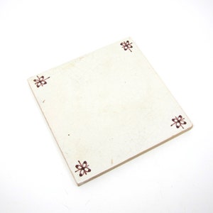 May include: A white ceramic tile with a brown floral design on each corner.