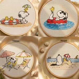 May include: Four circular wooden embroidery hoops containing cross-stitch patterns of Snoopy and Woodstock. The designs feature the characters in various summer beach scenes, including floating on a red life ring, sitting in a boat, lounging under umbrellas, and playing in the sand.