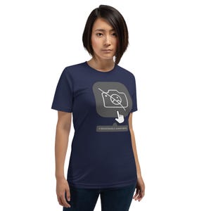 May include: Navy blue t-shirt featuring a graphic of a camera with a line through it, a hand pointing, and the text "A REASONABLE HUMAN BEING." The design is in white and gray. The shirt is a short-sleeved crew neck.