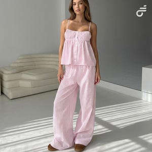 Puede incluir: Un conjunto de pijama de dos piezas a rayas rosas y blancas. La parte superior tiene botones en la parte delantera y tirantes finos. Los pantalones a juego son de pernera ancha. El conjunto está hecho de una tela ligera, perfecto para descansar o dormir.